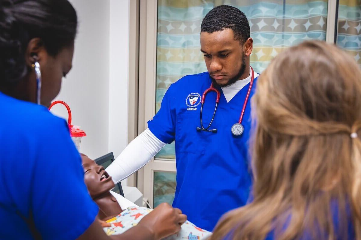 在模拟实验室里，一名护理专业的学生穿着蓝色的手术服在一个人体模型上工作